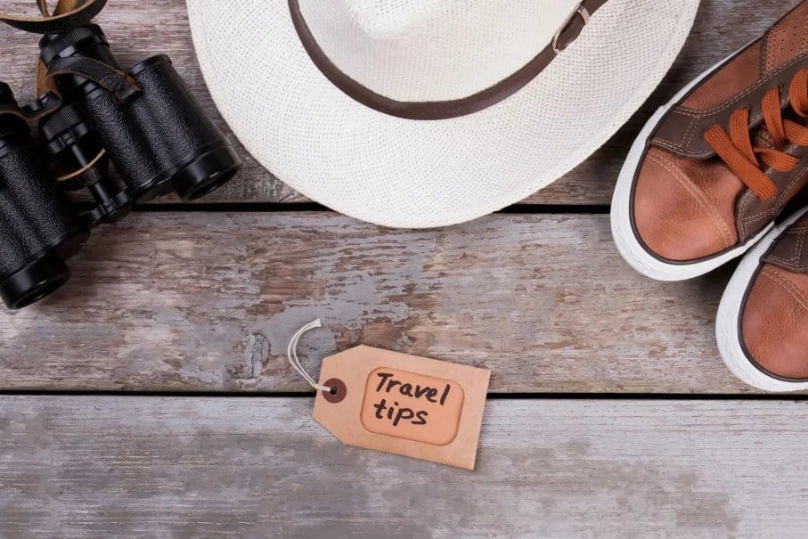 White hat, black binoculars, brown sneakers, and a tag reading "Travel tips" on a wooden surface.