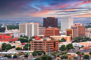 Downtown Albuquerque cityscape featuring mid-rise and high-rise office buildings under a colorful sunset sky, with residential areas and distant landscape in the background—perfect for your 2025 Vacation Guide.