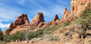 Red rock formations rise above desert vegetation under a blue sky with wispy clouds, capturing the stunning beauty of Sedona, Arizona—a must-see on any list of things to do in the region.